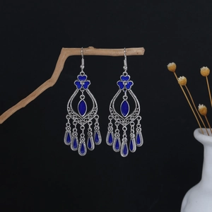 Detailed macro of Bohemian drop earrings with blue enamel and silver tassels on wood branch