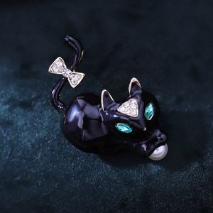 Detailed view of enamel black cat brooch with green gem eyes and a white pearl accent