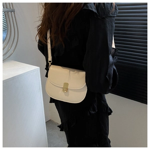 Detail of cream white saddle bag with gold buckle worn on shoulder against black outfit