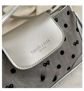 Détail du rabat argenté avec lettrage et tissu gris à pois noirs de ce sac