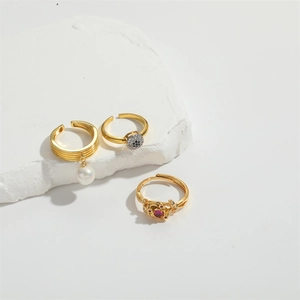 Detailed shot of gold plated snake rings with pearls and red gemstone on marble stone