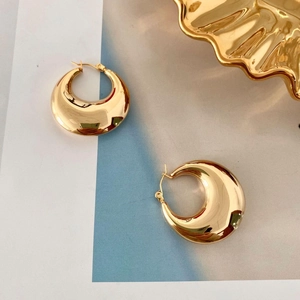 Macro shot of gold hollow teardrop earrings on a decorative wavy edge tray