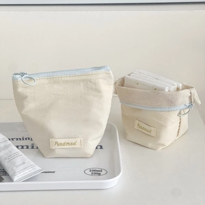 Detail of cream cosmetic pouches with blue zippers and brand label on a white tray