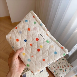 Close-up of quilted cream cosmetic bag with colorful polka dots held in hand