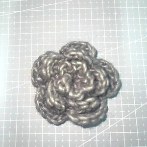 Detailed top view of a 7cm grey three-layer handmade crochet yarn flower on a cutting mat