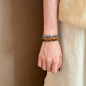 Three-piece layered beaded bracelet featuring blue stones and tiger eye with gold charms