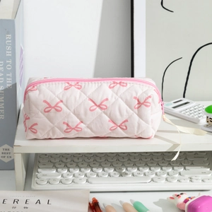 Close-up of pink quilted pencil case with bow pattern on desk with stationery