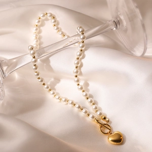 Elegant gold pearl necklace with heart pendant draped on silk background