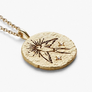 Macro detail of gold coin necklace with engraved bird pattern and shimmering small zircon stones