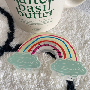 Detail view of a cute acrylic rainbow cloud hair claw clip on a white plush surface
