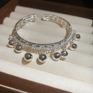 Gros plan des cloches argentées et de la texture métallique torsadée du bracelet