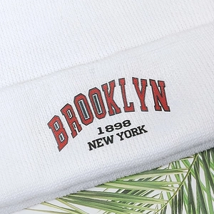 Close-up of white knit beanie featuring red Brooklyn 1898 New York embroidery detail