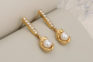 Close-up of long gold earrings with sparkling rhinestones and elegant round white pearls