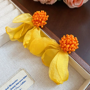 Detail view of bright yellow silk flower earrings with orange beaded stamens and soft fabric