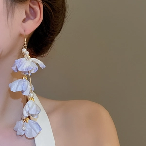 Détail de boucles d'oreilles à pompon avec pétales en tissu lilas et perles blanches