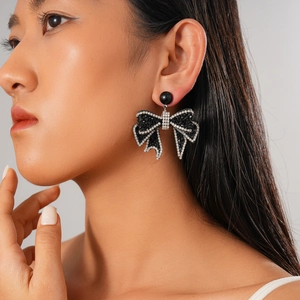 Close-up of black bow earrings with crystal accents worn by a model on a grey background