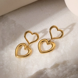 Detail of 18K gold-plated double heart earrings resting on a white marble stone