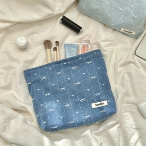 Detail of blue denim cosmetic bag with white bows and woven brand label on fabric