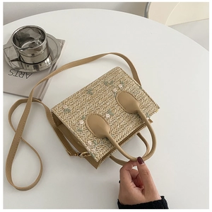 Detail of straw handbag featuring floral embroidery and brown PU trim on a white table