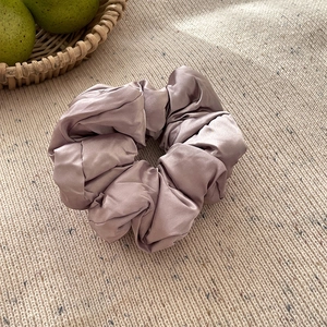 Détail d'un chouchou géant en soie rose sur tissu tricoté beige sous une lumière naturelle
