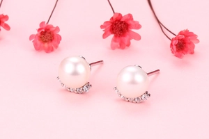 Macro shot of S925 silver pearl stud earring with sparkling cubic zirconia on pink background