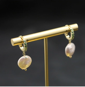 Detailed macro view of baroque pearl earrings with green emerald-like gemstone accents