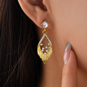 Close-up of golden rhinestone leaf earrings with crystal studs worn by a model