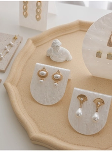 Detail view of gold metal earrings with faux pearls on marble acrylic display stands