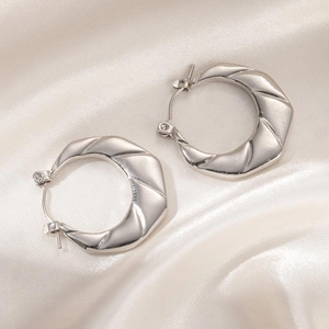 Detail of silver stainless steel textured earrings on a white silk fabric background