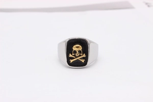 Macro detail of silver ring featuring a golden skull and crossbones on black background