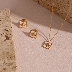 Detail of square shell pendant necklace and bee earrings set on a natural stone background