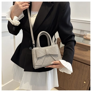 Close-up of a silver bow-accented crossbody bag with woven texture and top handles