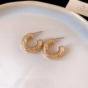 Detailed close-up of golden C-shaped spiral hoop earrings on a minimalist beige tray