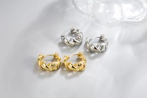 Detailed view of polished gold and silver twisted rope hoop earrings on silk fabric