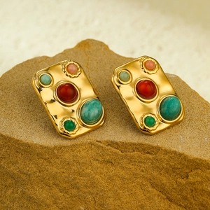 Exotic gold titanium earrings with square colorful gemstones on a natural rock background