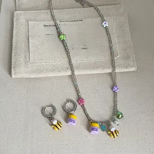 Detail of beaded necklace and hoop earrings with bee and honey pot charms on fabric