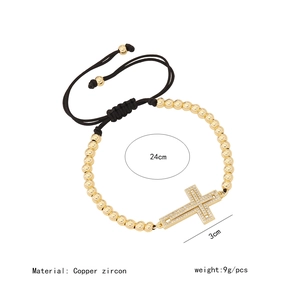 Detail of 18K gold beaded bracelet with zircon cross charm and adjustable black cord