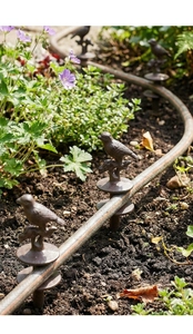 Detailed view of vintage cast iron bird hose guide stake in an outdoor garden setting