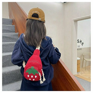 Detail of red strawberry chest bag for kids featuring white zipper tassel and canvas fabric
