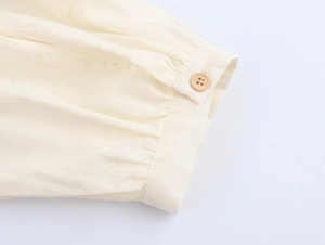 Macro shot of ivory blouse cuff showing wood button detail and pleated cotton-linen fabric