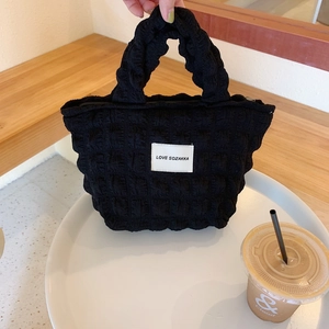 Detail of black bubble texture canvas handbag with zipper and signature logo label