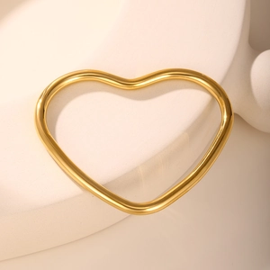 Detailed view of heart-shaped gold bangle on minimalist stone pedestal with warm lighting