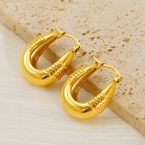 Détail de boucles d'oreilles dorées en U avec texture diamant sur pierre et tissu soie