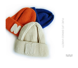Detailed knit texture of colorful children's beanies with plush N letter embroidery