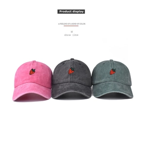 Detailed embroidery of a red strawberry on vintage washed cotton baseball caps in three colors