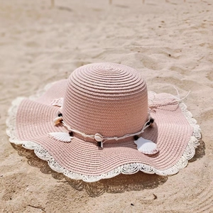 Pink straw sun hat with shell band and white lace trim on a sunny sandy beach