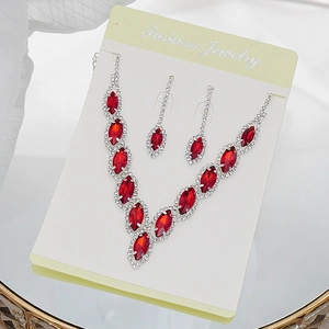 Macro detail of elegant V-shaped red crystal necklace and earring set on white card