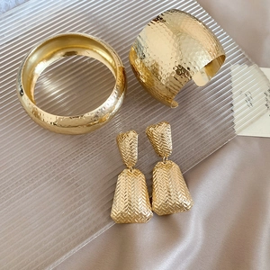 Detail of gold metal jewelry set with hammered texture and woven pattern on champagne silk