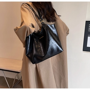 Side view of a large black glossy leather tote bag styled with a khaki trench coat