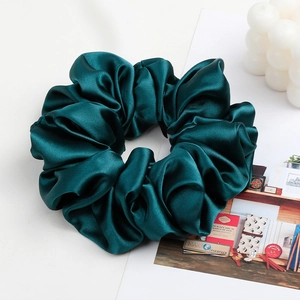 Close-up of emerald green satin scrunchie with elegant folds and glossy texture